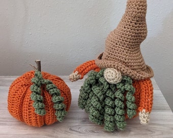 May include: A crocheted gnome with a brown hat and green beard, holding a crocheted orange pumpkin.