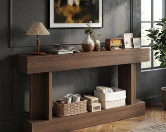 May include: A dark wood console table with a rectangular top and two thick vertical supports. The table features a lower shelf holding a woven basket, two small stacked wooden boxes, and a white fabric-lined storage bin.