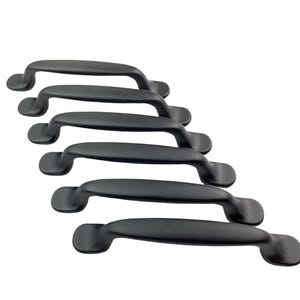 May include: Five black cabinet pulls or handles in a staggered stack. The pulls are made of metal and have a simple, rounded design.