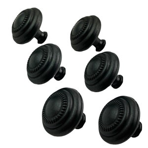 May include: Six black cabinet knobs with a raised, circular design. The knobs have a slightly textured finish.