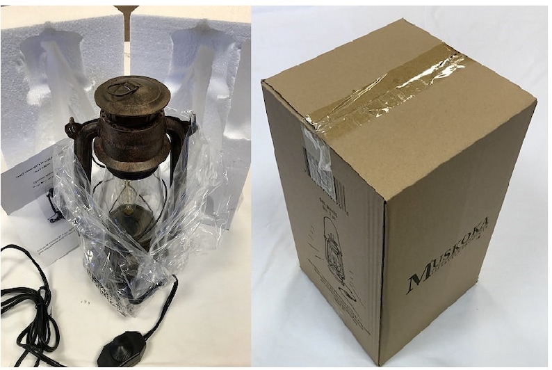 Pu&ograve; includere: Una lanterna in metallo marrone con un camino in vetro trasparente e un cavo di alimentazione nero con interruttore dimmer, parzialmente avvolta in plastica e schiuma. Accanto c'&egrave; una scatola di cartone marrone con l'etichetta Muskoka.