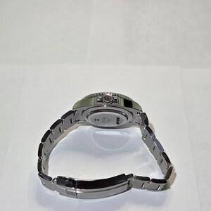 May include: A silver-toned stainless steel wristwatch with a metal link bracelet. The back of the watch case features engraved text that reads HCLAND and HILL, along with a small logo. The watch is shown from an angled perspective.