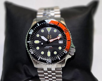 May include: An automatic diver's watch with a black dial, luminous circular indices, and a date window at the three o'clock position. The bezel features a black and orange insert with white numerals. It has a stainless steel link bracelet.