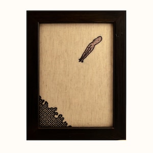 May include: A framed artwork with a black and white embroidered design of an octopus on a beige background.