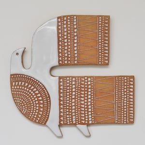 May include: A ceramic wall hanging in the shape of a bird. The bird has a white head and body with a brown patterned design on the lower body and wings. The design includes geometric shapes and lines.
