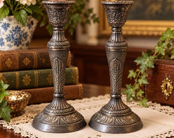 Puede incluir: Un par de candelabros de metal plateado a juego con intrincados patrones florales y de hojas en relieve, una columna central texturizada y una base circular ancha con detalles decorativos en los bordes y un acabado desgastado.