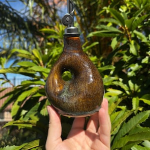 Può includere: Un'oliera in ceramica smaltata marrone con un corpo arrotondato e asimmetrico caratterizzato da un'impugnatura centrale circolare. Il contenitore è dotato di un beccuccio in metallo argentato con tappo incernierato per versare.