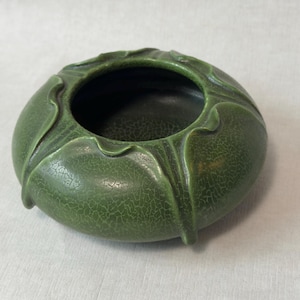 May include: A round, low-profile ceramic bowl in a deep forest green hue. The exterior features a distinct crackle glaze finish and raised, petal-like vertical ridges that extend from the central opening toward the base of the vessel.