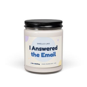 May include: A clear glass candle jar with a black lid containing white wax. The label features a light blue circle and the text: SMELLS LIKE I Answered the Email, A for Adulting, HAND-POURED SOY, 9 OZ. The design includes small pastel dots.