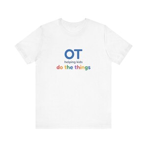 May include: A white short-sleeve t-shirt featuring the blue text OT, followed by the words helping kids in dark blue, and the words do the things in multicolored letters including red, yellow, green, and blue on the front center.