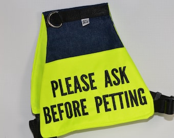 Könnte beinhalten: Eine leuchtend gelbe Hundeweste mit schwarzem Text, der "PLEASE ASK BEFORE PETTING" lautet. Die Weste hat einen schwarzen Gurt und einen silbernen Ring.