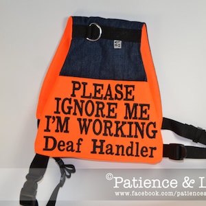 May include: Orange vest with black text that reads "Please Ignore Me I'm Working Deaf Handler". The vest has a black strap and a blue denim patch on the back.