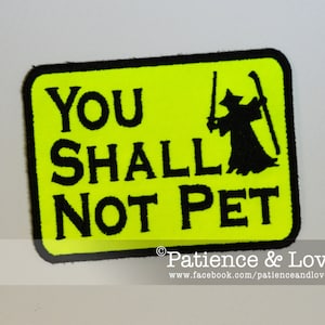 May include: A yellow patch with black text and a black silhouette of a figure holding a staff. The text reads "You Shall Not Pet".