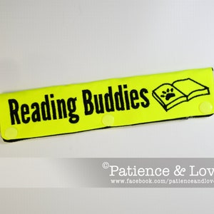 Peut inclure: Un marque-page en tissu jaune avec du texte noir qui dit "Reading Buddies". Le marque-page a une empreinte de patte noire à l'intérieur d'une illustration de livre noir. Le marque-page a une petite étiquette blanche avec le texte "Love" dessus.