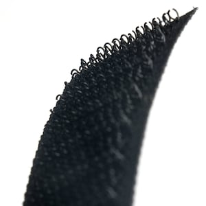 May include: Close-up of black hook and loop fastener tape. The tape has a textured surface with small loops.