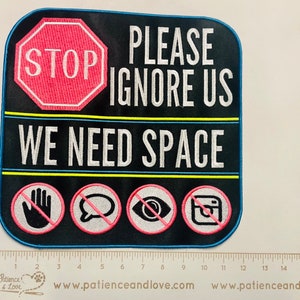 May include: A black and white sign with a red stop sign in the top left corner. The sign says "STOP PLEASE IGNORE US WE NEED SPACE". There are four icons below the text: a hand with a line through it, a speech bubble with a line through it, an eye with a line through it, and an Instagram logo with a line through it.