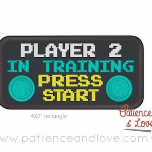 Può includere: Un cerotto ricamato nero e grigio con il testo "PLAYER 2 IN TRAINING PRESS START" in font pixelato bianco, giallo e blu. Due pulsanti pixelati blu e bianchi sono su entrambi i lati del testo. Il cerotto misura 4x2 pollici.