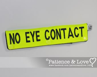 May include: A neon yellow rectangular accessory with the words "NO EYE CONTACT" in bold black letters. The accessory has a small white tag with the word "LOVE" printed on it. The item is likely a novelty item or a gag gift.