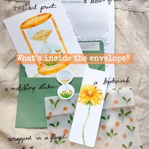 May include: An art print, sticker, and bookmark are wrapped in floral tracing paper. The art print is 5x7 inches and features an hourglass design. A letter is also included. The text on the image says "What's inside the envelope?"