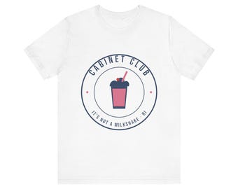 May include: A white short-sleeved t-shirt featuring a circular logo on the chest. The logo contains a pink drink with a straw and a cherry, surrounded by the text CABINET CLUB and IT'S NOT A MILKSHAKE · RI in dark blue lettering.