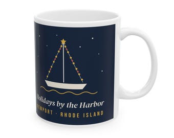 May include: A white ceramic mug featuring a dark blue background with a graphic of a sailboat decorated with lights and a star. The text reads Holidays by the Harbor, Newport, Rhode Island in white and gold lettering.