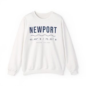 Może przedstawiać: Kremowa bluza z okrągłym dekoltem i ciemnoniebieskim napisem NEWPORT, falistą linią, współrzędnymi 41.49 N / 71.31 W oraz słowami RHODE ISLAND wydrukowanymi mniejszą czcionką poniżej współrzędnych.