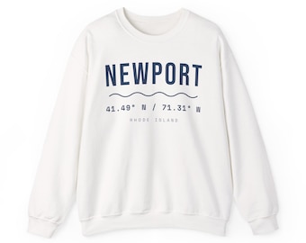 Peut inclure: Un sweat-shirt à col rond couleur crème avec le texte bleu foncé NEWPORT, une ligne ondulée, les coordonnées 41.49 N / 71.31 W et les mots RHODE ISLAND imprimés en plus petite police sous les coordonnées.