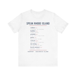 May include: A white short-sleeve t-shirt featuring the text SPEAK RHODE ISLAND in dark blue. Below, a list of local terms and definitions includes cabinet, bubbler, grindah, packy, wicked, the bridge, and locals summer, ending with NEWPORT - AQUIDNECK ISLAND.