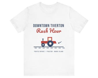 May include: A white short-sleeve t-shirt featuring the text DOWNTOWN TIVERTON Rush Hour in blue and red. Below the text is a graphic of a red and blue tractor on a road, with the text TRAFFIC REPORT: 1 TRACTOR RHODE ISLAND at the bottom.