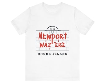 May include: A white short-sleeve t-shirt featuring a graphic of a cartoon character peeking over a brick wall. The red text reads NEWPORT WAZ 'ERE, with the words RHODE ISLAND printed in black block letters underneath the brick wall design.