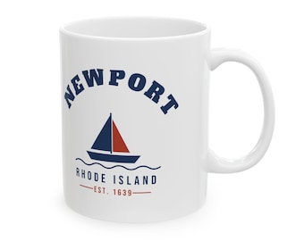 May include: A white ceramic mug featuring a navy blue and red graphic of a sailboat on waves. The text reads NEWPORT in an arch above the boat, with RHODE ISLAND and EST. 1639 printed in navy blue and red below the sailboat design.