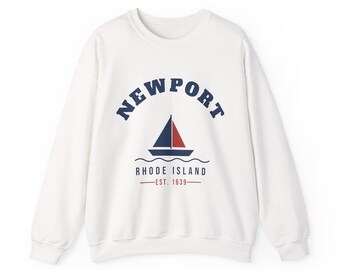 Puede incluir: Una sudadera blanca de manga larga con cuello redondo que presenta un gráfico azul marino de un velero sobre líneas onduladas. El texto dice NEWPORT en arco, RHODE ISLAND debajo del barco y EST. 1639 en rojo con líneas horizontales.