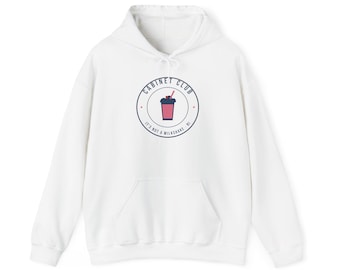 Puede incluir: Una sudadera blanca de manga larga con capucha y un gráfico circular en el pecho. El logotipo muestra una bebida rosa en un vaso azul oscuro con una pajita, rodeado por el texto CABINET CLUB y IT'S NOT A MILKSHAKE.