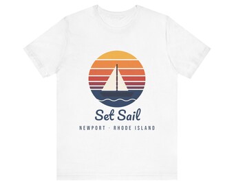 Peut inclure: Un t-shirt blanc à manches courtes avec un motif circulaire représentant un voilier sur l'eau devant un coucher de soleil aux rayures orange, rouges et violettes. Le texte Set Sail et NEWPORT · RHODE ISLAND est inscrit dessous.