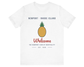 May include: A white short-sleeve t-shirt featuring a graphic of a yellow pineapple with green leaves. Text reads: NEWPORT RHODE ISLAND, Welcome, THE NEWPORT SIGN OF HOSPITALITY, EST. 1639. The design is centered on the chest of the garment.