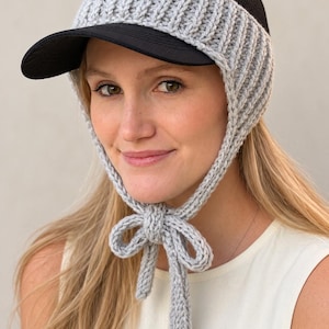 May include: A black baseball cap featuring a light gray crocheted earflap attachment that wraps around the sides and secures under the chin with a matching gray crocheted tie. The cap has a solid black brim and a black mesh crown.