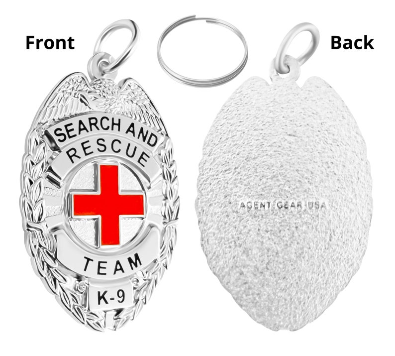 Op de afbeelding: Zilverkleurige metalen sleutelhanger met een zoek- en reddingsbadge. De badge heeft een rood kruis, de woorden "Search and Rescue", "Team" en "K-9", en een laurierkransontwerp. De achterkant van de sleutelhanger is effen met de woorden "Agent Gear USA" erop gegraveerd.