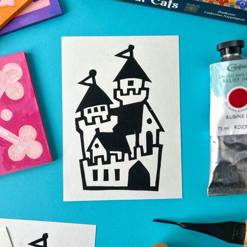 May include: Black and white illustration of a castle with multiple towers and a gate. The illustration is printed on a white card.