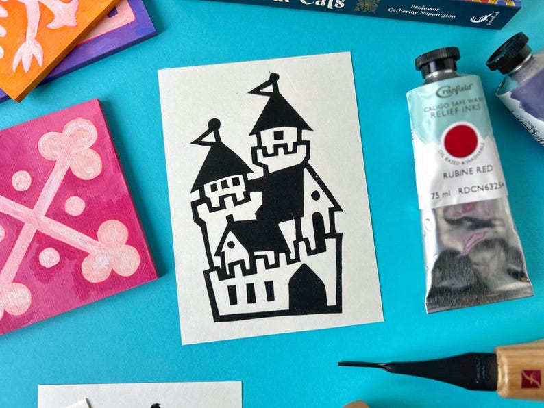 May include: A black and white illustration of a castle on a white card. The castle is a simple design with a tall tower and a few smaller towers. The illustration is surrounded by a white border.