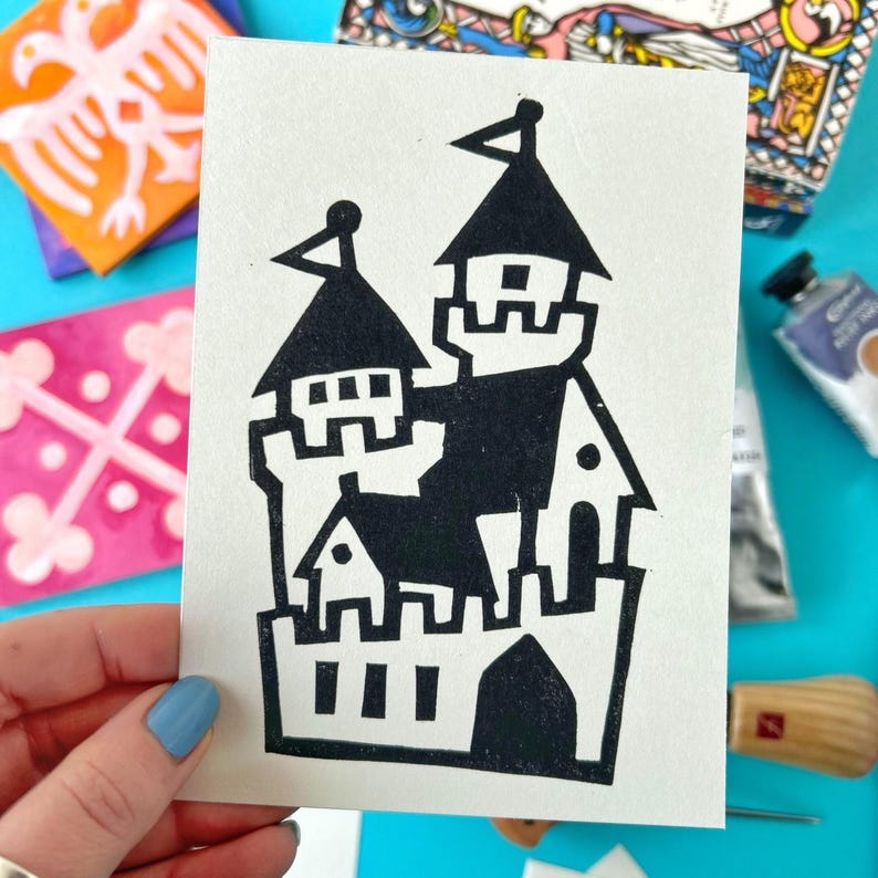 May include: Black and white linocut print of a castle with multiple towers and a gate. The castle is on a white card.