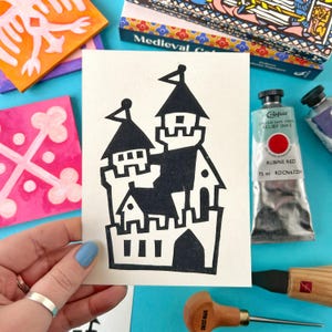 May include: A black and white illustration of a castle on a white card. The castle is made up of multiple towers and has a simple, blocky design.