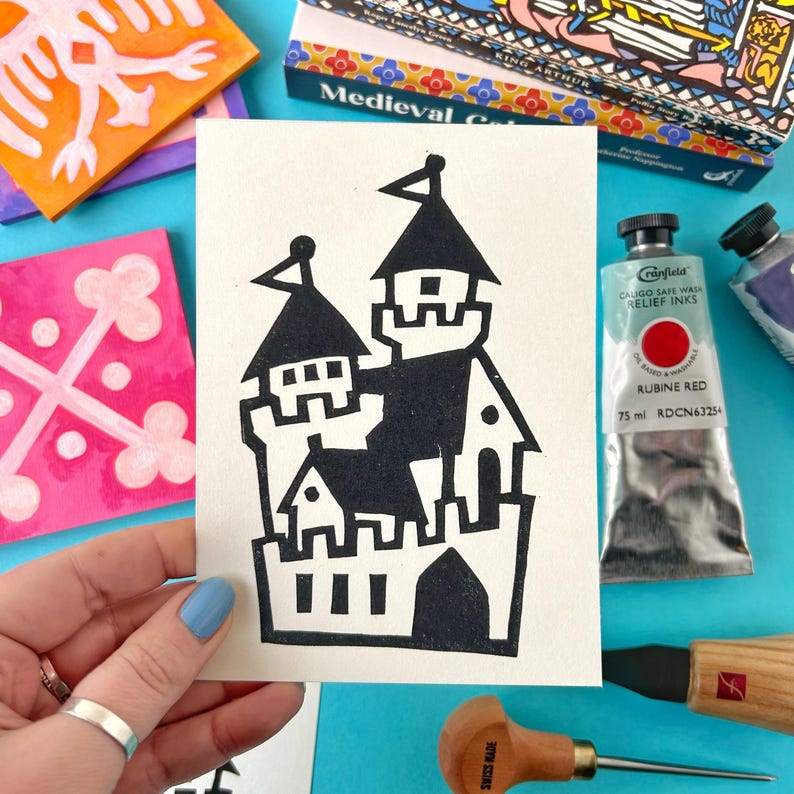 May include: A black and white illustration of a castle on a white card. The castle is made up of multiple towers and has a simple, blocky design.