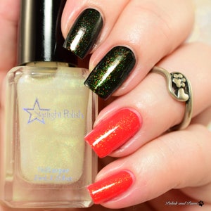May include: A bottle of Starlight Polish nail lacquer next to a hand with painted nails. Two nails are painted a dark green with glitter, and two are painted a bright red with glitter. A silver ring with a paw print design is on the ring finger.