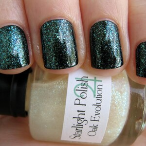 May include: A bottle of Starlight Polish nail polish in the color Oak Evolution. The polish is a light, shimmery white with a green glitter finish. The bottle is shown with a hand wearing the polish on all five fingernails.
