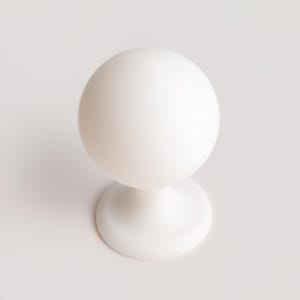 May include: A solid white cabinet knob featuring a smooth spherical head attached to a circular base. The hardware has a matte finish and a clean, uniform appearance, designed for attachment to furniture doors or drawer fronts.