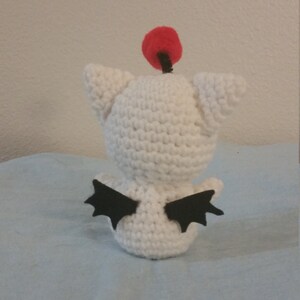 Puede incluir: Juguete de peluche blanco tejido a crochet con alas negras y un pomp&oacute;n rojo en la parte superior de la cabeza.