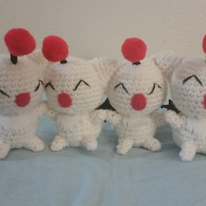 May include: Four white crocheted plush toys with red and black accents. Each toy has a red pom-pom on top of its head and black eyes. The toys are smiling and have red noses.