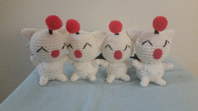Puede incluir: Cuatro peluches blancos de ganchillo con detalles rojos y negros. Cada juguete tiene un pomp&oacute;n rojo en la parte superior de la cabeza y ojos negros. Los juguetes sonr&iacute;en y tienen narices rojas.
