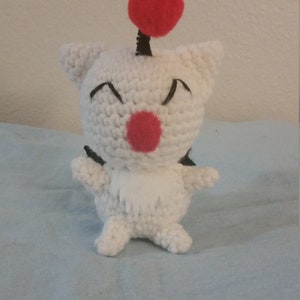 Puede incluir: Juguete de peluche blanco tejido a crochet con un pomp&oacute;n rojo en la parte superior de la cabeza. El juguete tiene ojos negros y una nariz roja.