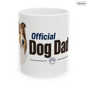 May include: A white ceramic mug featuring a detailed illustration of a brown and white collie dog on the left side. The text "Official Dog Dad" is printed in dark blue and brown, accompanied by a small blue paw print graphic below.